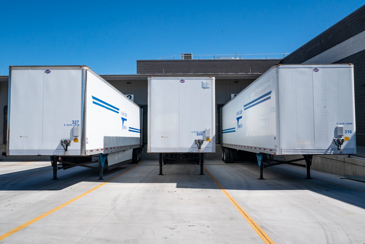 about-us-02 Three white cargo trailers parked at an industrial shipping dock under clear blue skies.